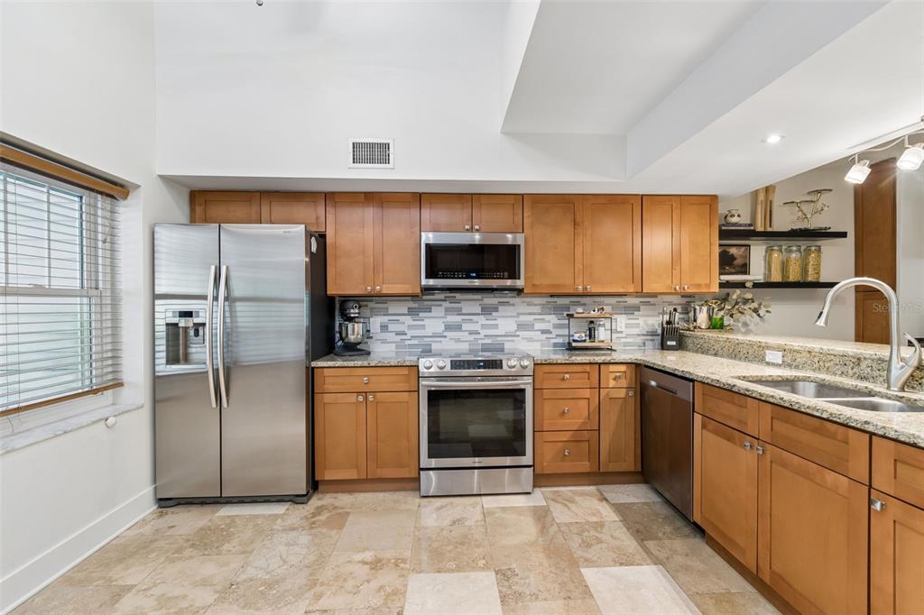 A kitchen features wood cabinets, granite countertops, stainless steel appliances, and a tiled floor — 2599 DOLLY BAY DRIVE UNIT 302, PALM HARBOR, FL