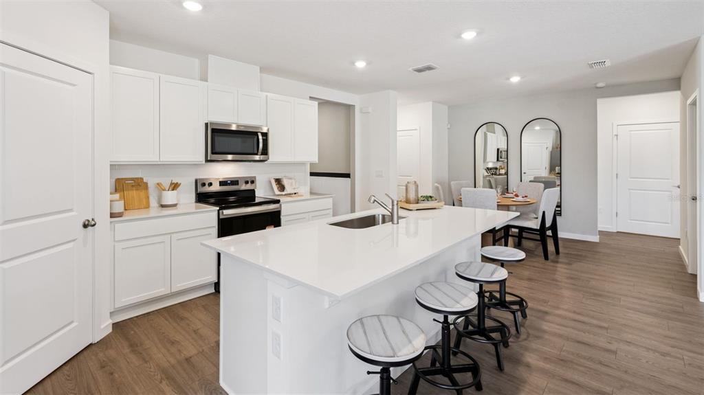 A modern kitchen features white cabinetry, a central island with bar stools, and wood flooring — 1864 SOUTHBURY DRIVE, KISSIMMEE, FL