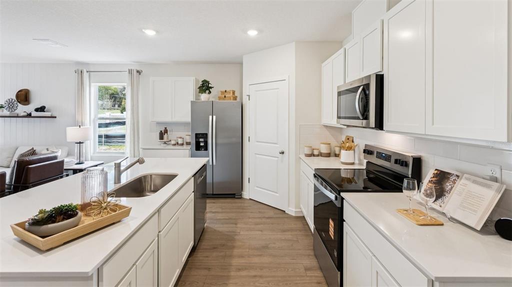 A modern kitchen features white cabinets, stainless steel appliances, a large island, and wood-look flooring — 1864 SOUTHBURY DRIVE, KISSIMMEE, FL