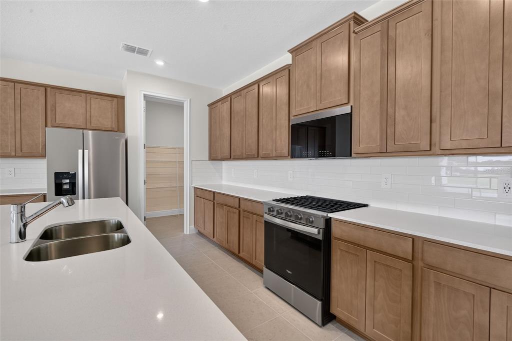 A modern kitchen features brown wood cabinets, white countertops, stainless steel appliances, and a range hood — 12907 PIERCE STREET, PARRISH, FL