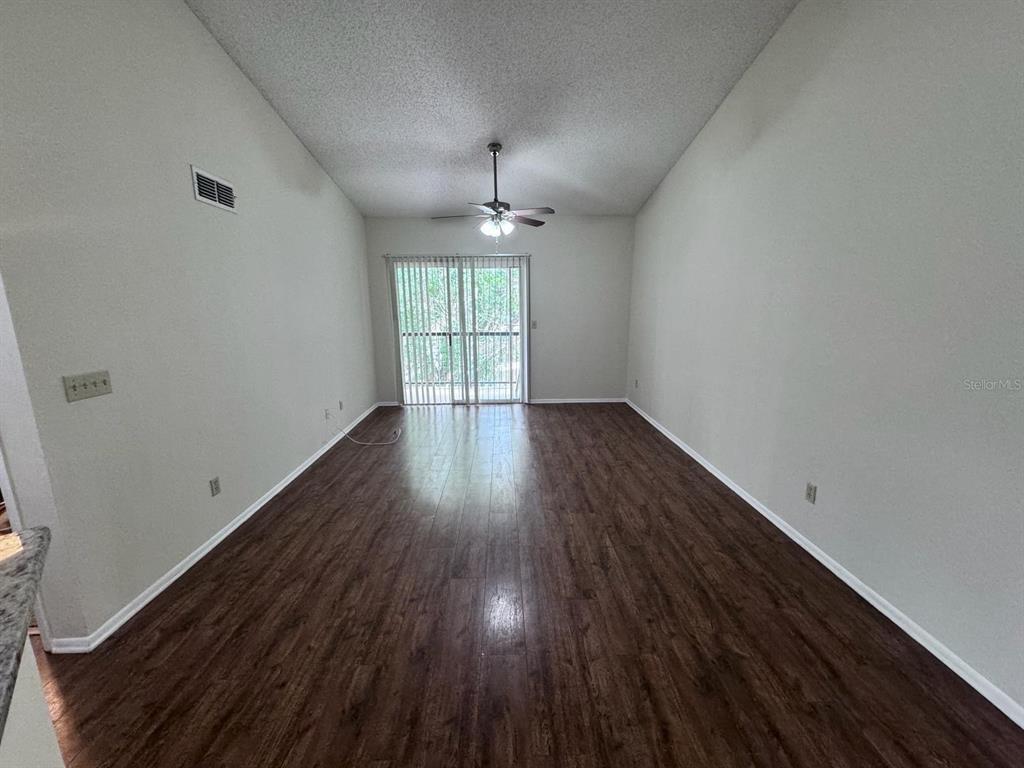 An empty living room features dark wood-look flooring, light walls, and a ceiling fan — 1972 LAKE ATRIUMS CIRCLE UNIT 199, ORLANDO, FL
