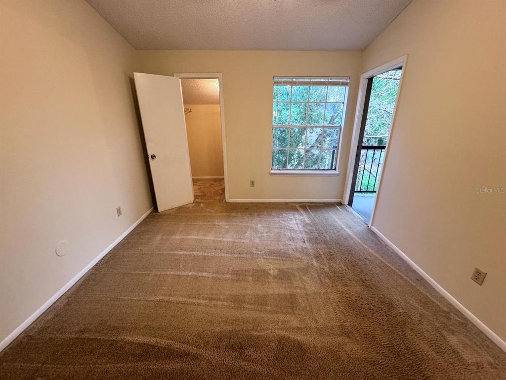 A bedroom with beige carpet, a closet, a window, and a door leading to a balcony — 1972 LAKE ATRIUMS CIRCLE UNIT 199, ORLANDO, FL