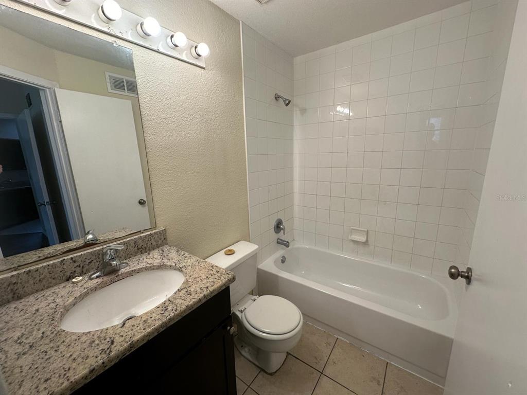 A bathroom featuring a granite vanity, a toilet, and a white tiled shower-tub combination — 1972 LAKE ATRIUMS CIRCLE UNIT 199, ORLANDO, FL