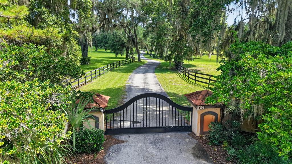 A black metal gate stands at the entrance of a long driveway lined with trees — 11105 W HIGHWAY 326, OCALA, FL