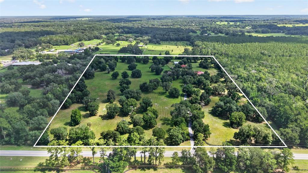 An aerial view shows a large, tree-dotted grassy lot outlined in white near a road — 11105 W HIGHWAY 326, OCALA, FL
