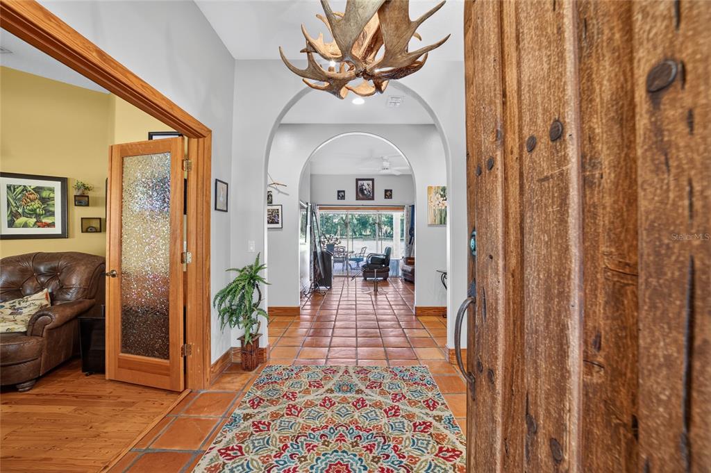 An entryway features a rustic wooden door, terracotta tile flooring, and an antler chandelier — 11105 W HIGHWAY 326, OCALA, FL
