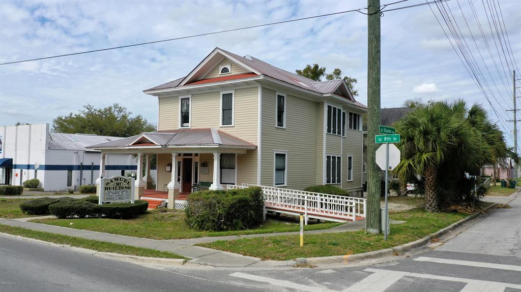 A two-story, light-yellow house with a front porch and a wheelchair ramp sits on a corner — 151 SE 8TH STREET, OCALA, FL