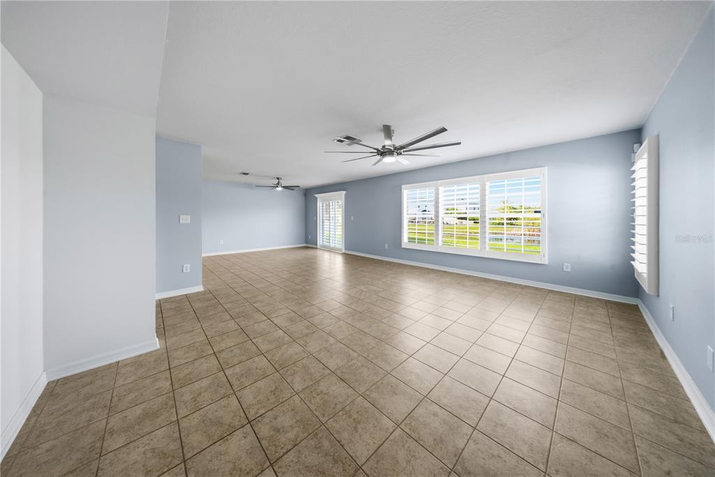 An empty living room with light blue walls, tan tile flooring, and two ceiling fans — 9515 SIMEON DRIVE, LAND O LAKES, FL