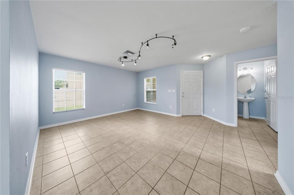 An empty room with light blue walls, tile flooring, track lighting, and an attached bathroom — 9515 SIMEON DRIVE, LAND O LAKES, FL