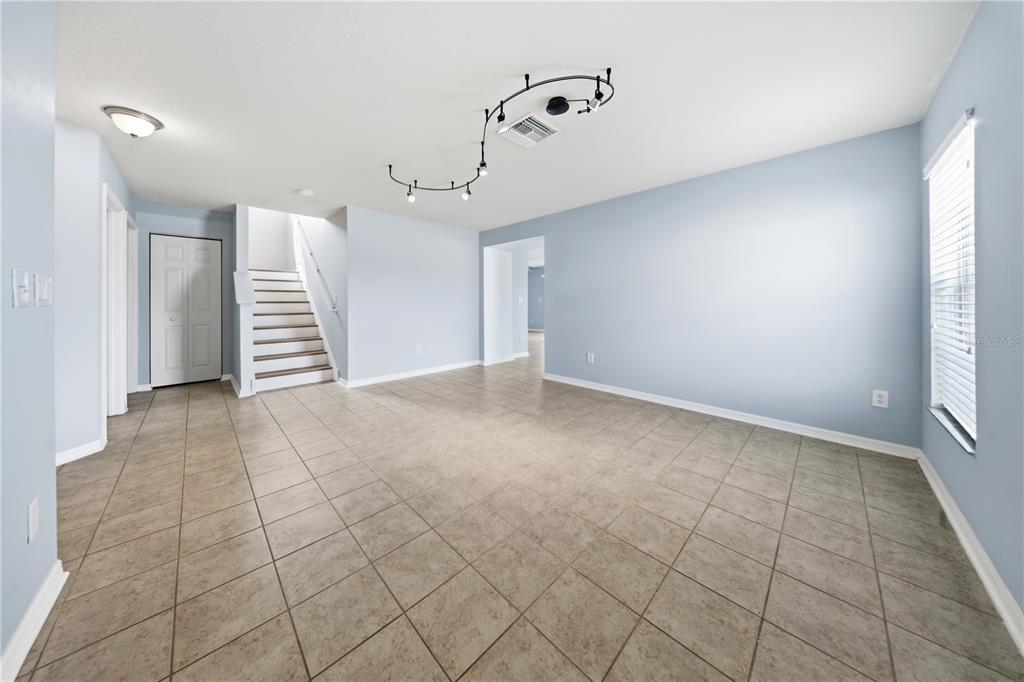A bright living room features light blue walls, tile flooring, a staircase, and track lighting — 9515 SIMEON DRIVE, LAND O LAKES, FL
