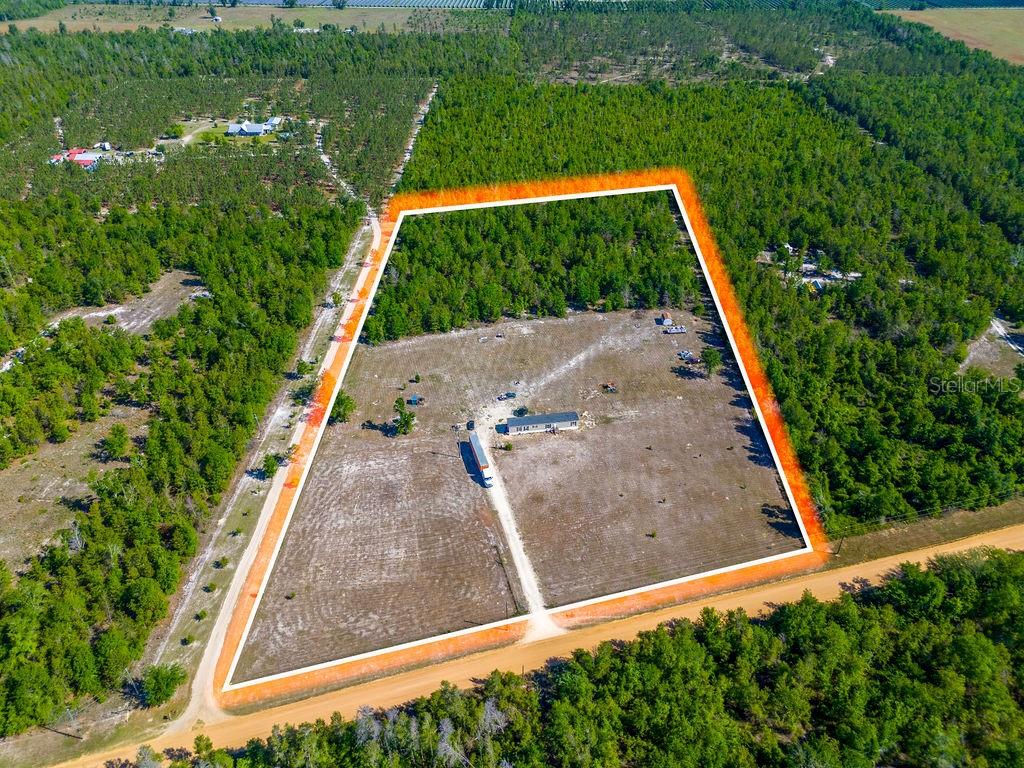 A long, single-story manufactured home with gray siding sits on a sandy, open lot — 1147 SE HAMMERLY STREET, MADISON, FL
