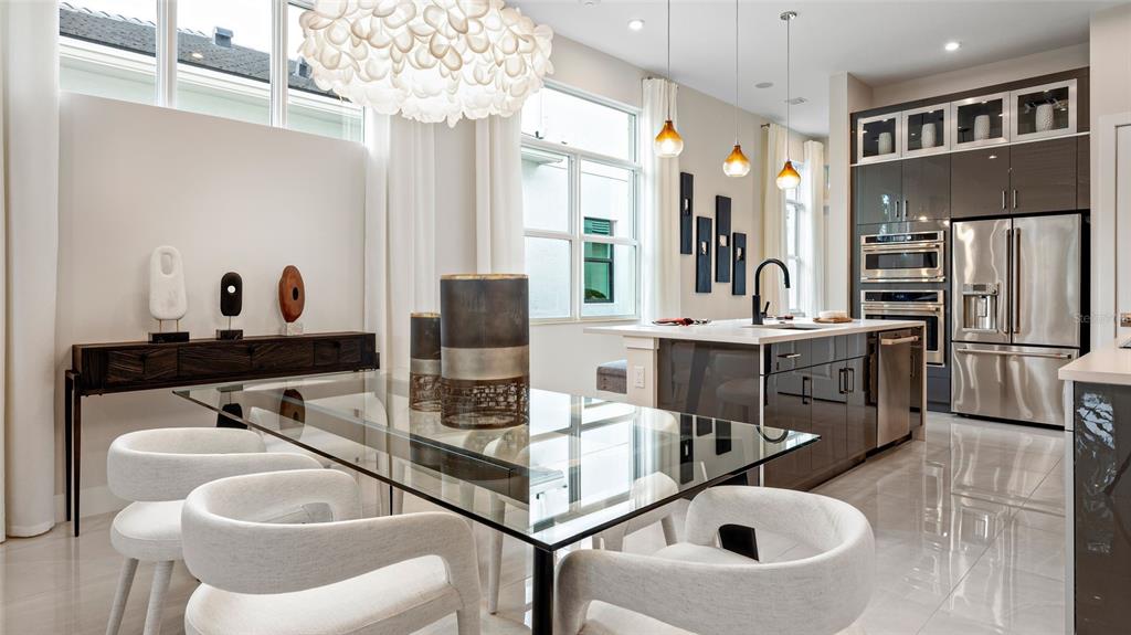 A modern dining area with a glass table and white chairs sits beside a kitchen — 1580 BELLAGIO LOOP, TAVARES, FL