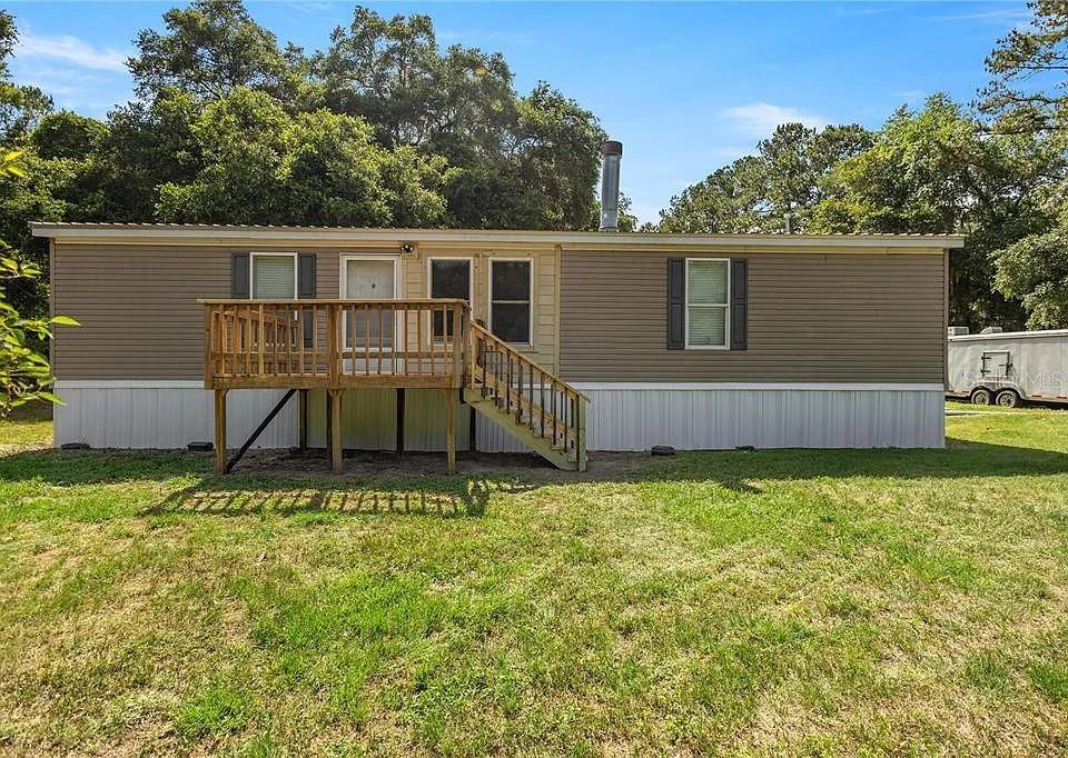 A single-story manufactured home with tan siding, a wooden deck, and a metal chimney — 15340 NW 65TH AVENUE ROAD, REDDICK, FL
