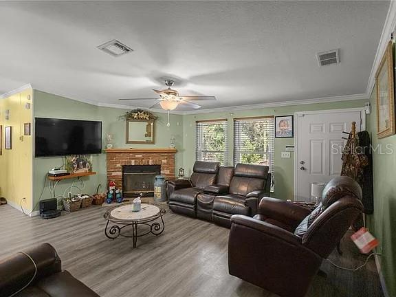 A living room features a brick fireplace, leather furniture, a ceiling fan, and wood-look flooring — 15340 NW 65TH AVENUE ROAD, REDDICK, FL