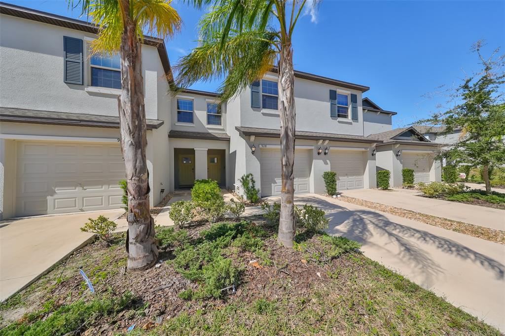 A row of two-story townhomes with beige stucco facades, attached garages, and palm trees — 928 ROYAL EMPRESS DRIVE, RUSKIN, FL