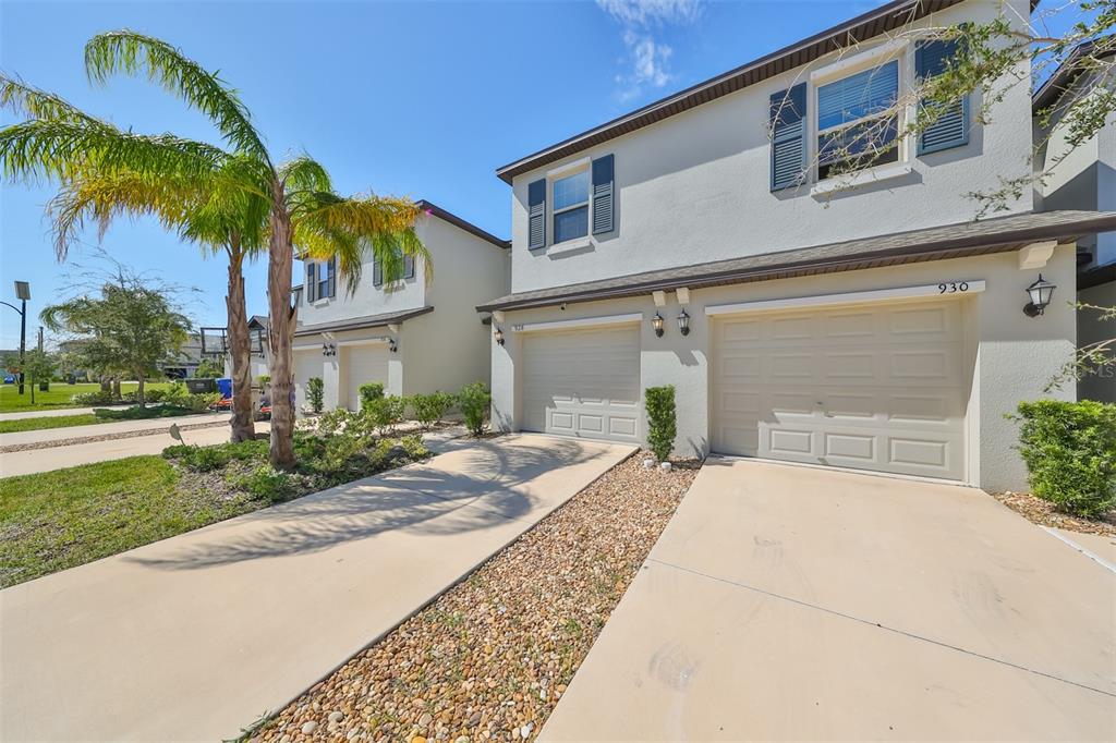 A two-story townhouse exterior features a two-car garage, light stucco walls, and a palm tree — 928 ROYAL EMPRESS DRIVE, RUSKIN, FL