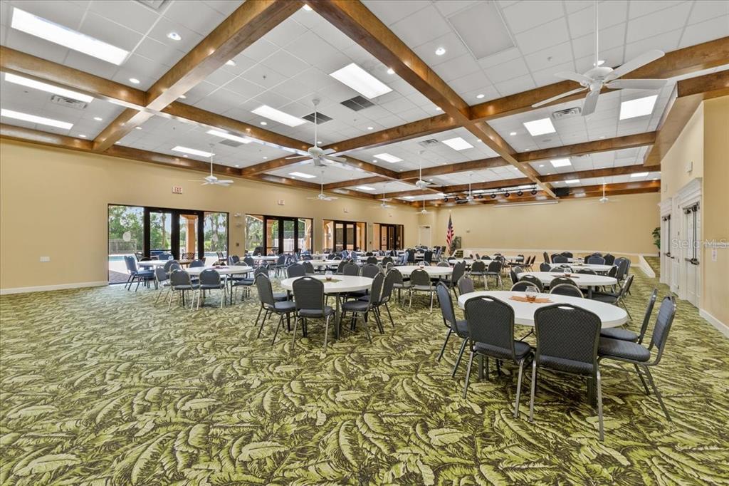 A large event hall features round tables, dark chairs, a patterned carpet, and exposed ceiling beams — 110 LAYNEWADE ROAD, POLK CITY, FL