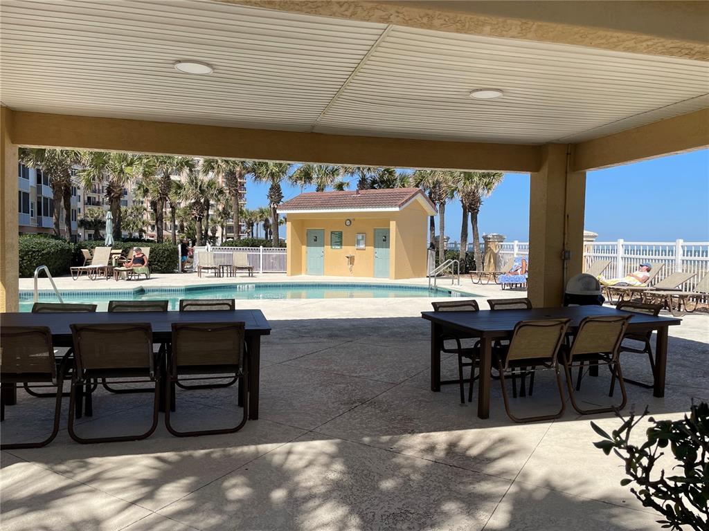 A covered patio area features two dining tables overlooking an outdoor swimming pool and building — 3651 S CENTRAL AVE UNIT 312, FLAGLER BEACH, FL