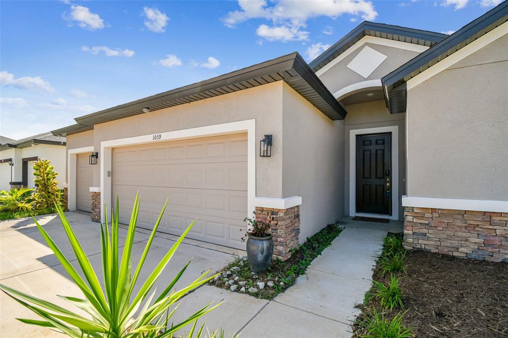 A beige single-story house exterior features a two-car garage, stone accents, and a dark door — 1039 DAVIS HEATHER CIRCLE, SEFFNER, FL
