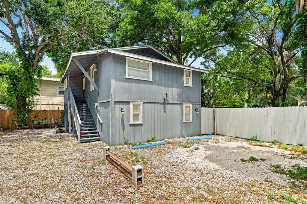 The exterior of a two-story gray house with a gravel yard and wooden fencing — 4834 TAYLOR STREET N, ST PETERSBURG, FL