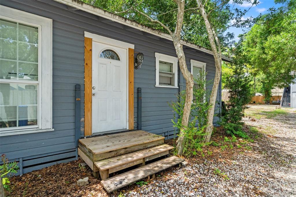 A two-story grey house with an exterior staircase stands on a gravel lot — 4834 TAYLOR STREET N, ST PETERSBURG, FL