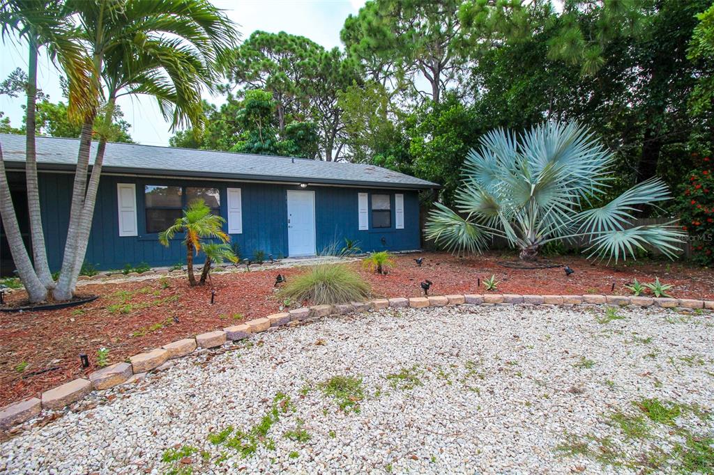 A blue single-story house features a gravel driveway, palm trees, and a stone border — 1116 ROYAL ROAD, VENICE, FL