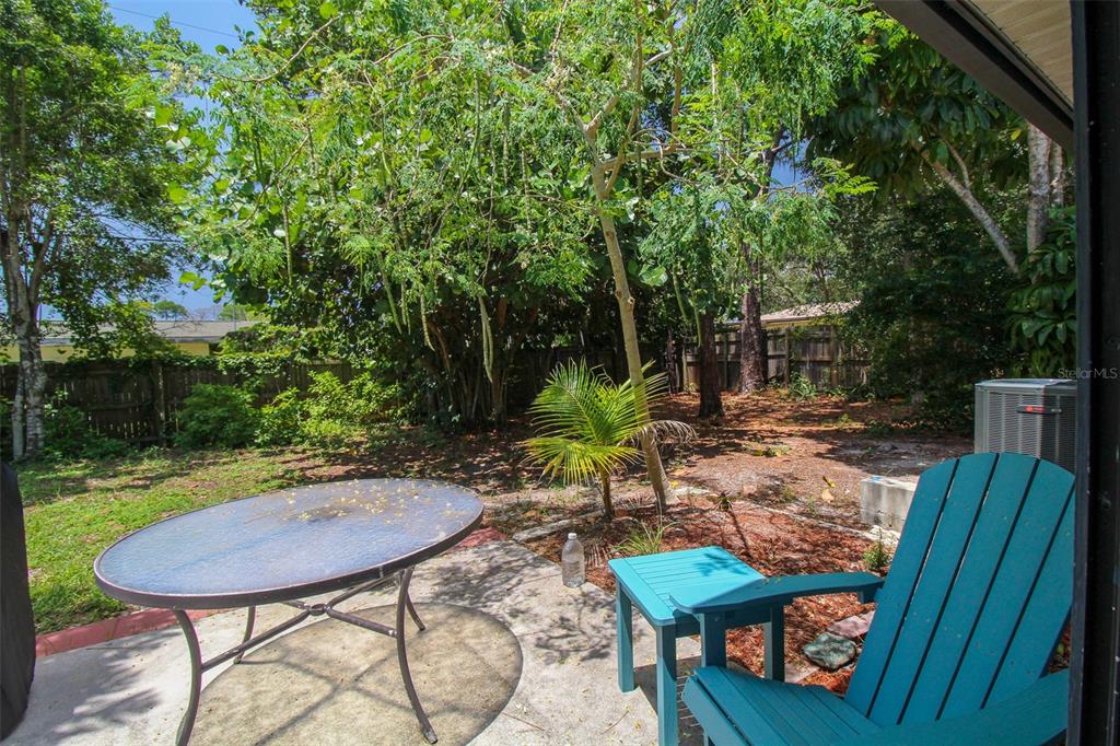 A patio with a glass-topped table and a teal chair overlooks a wooded backyard — 1116 ROYAL ROAD, VENICE, FL