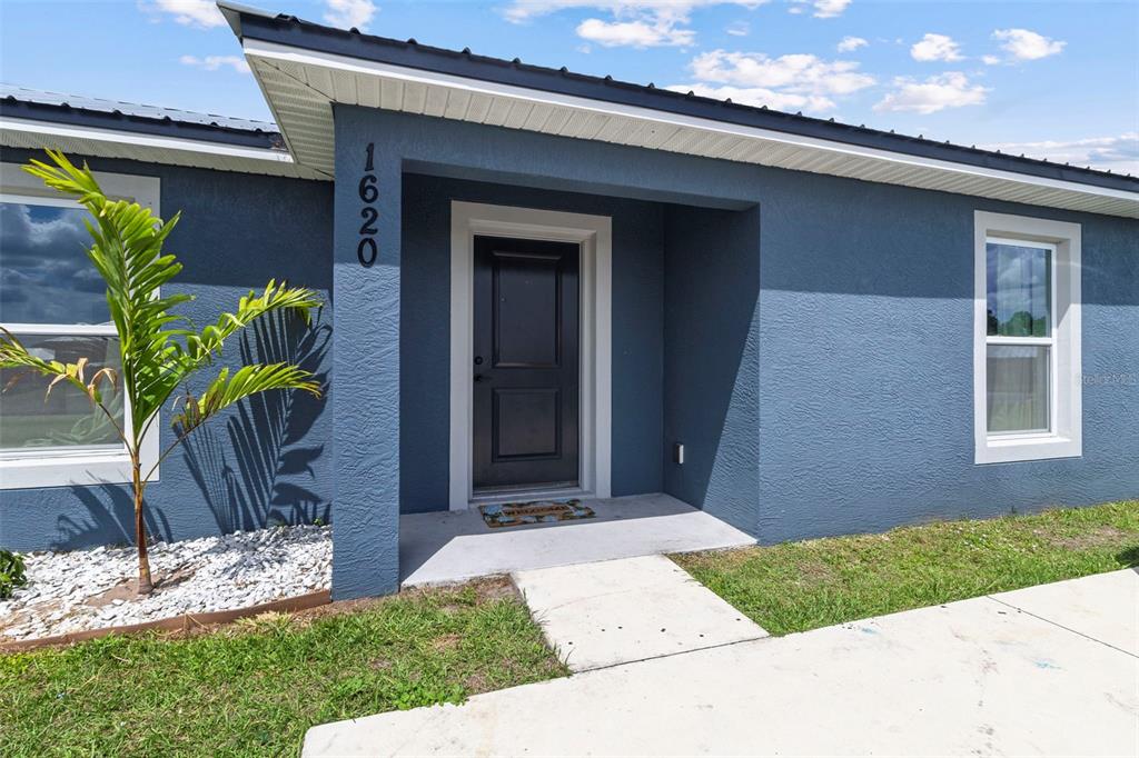 The exterior of a blue house features a black front door and a concrete walkway — 1620 SE HAVEN DRIVE, ARCADIA, FL