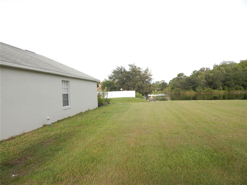 A side view of a house exterior with a grassy yard leading to a pond — 3434 CYPRESS POINT CIRCLE, ST CLOUD, FL