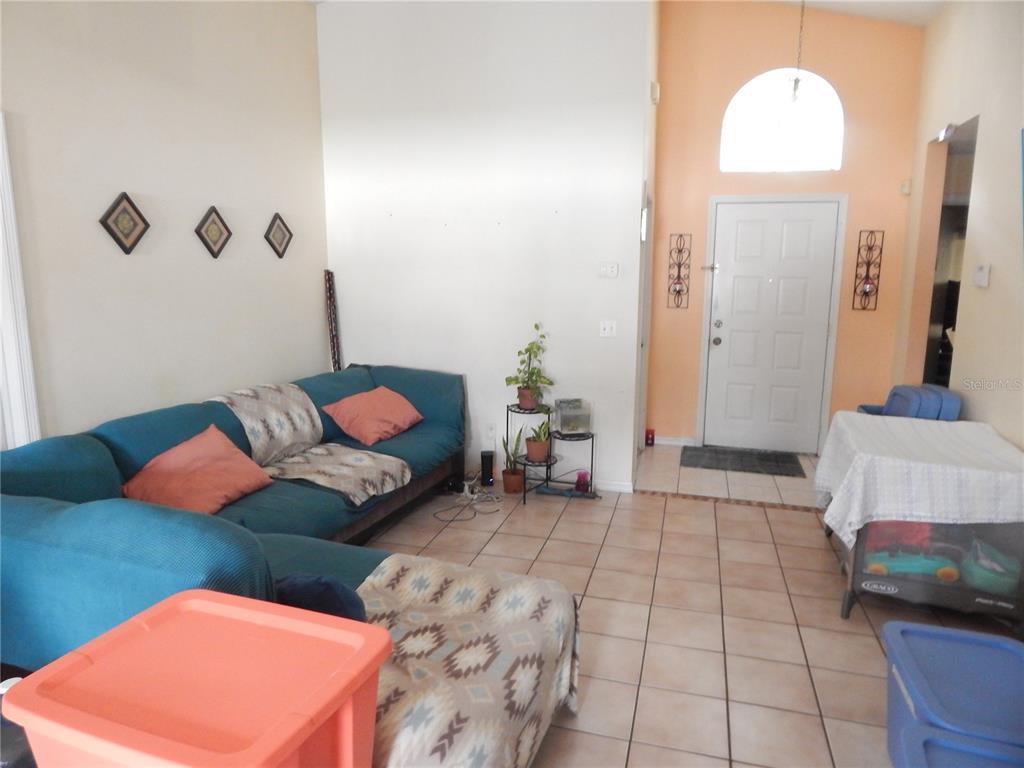 A living room with tile floors, a blue sectional sofa, and a front entryway door — 3434 CYPRESS POINT CIRCLE, ST CLOUD, FL