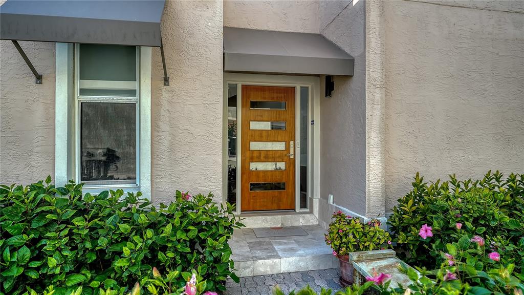 A modern wood front door with horizontal glass panels sits under a gray metal awning — 3530 MISTLETOE LANE, LONGBOAT KEY, FL