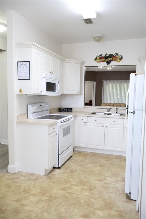 A kitchen features white cabinets, a white stove, a microwave, and beige laminate countertops — 8842 CORAL PALMS COURT UNIT B, KISSIMMEE, FL