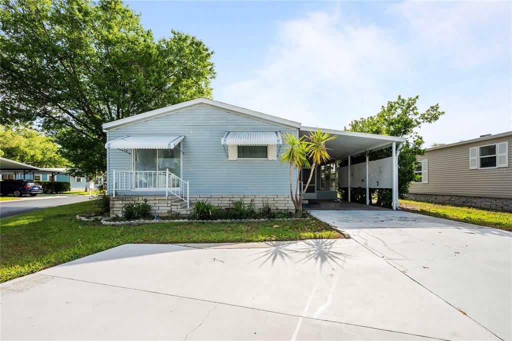 An exterior view of a light blue manufactured home with a carport and concrete driveway — 3210 HICKORY DRIVE, WESLEY CHAPEL, FL