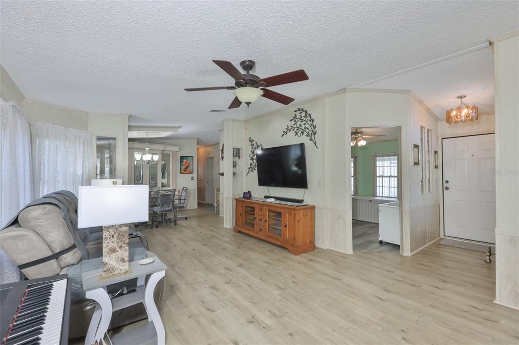 A living room features light wood-look flooring, a ceiling fan, and a wall-mounted television — 192 S PORT ROYAL LANE, APOLLO BEACH, FL