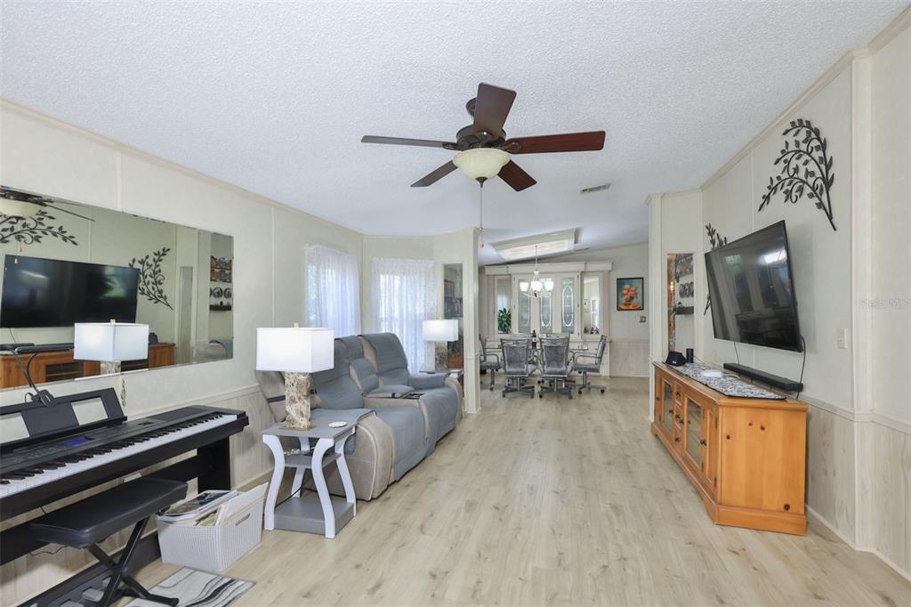 A living room with light wood flooring, a ceiling fan, a piano, and a dining area — 192 S PORT ROYAL LANE, APOLLO BEACH, FL