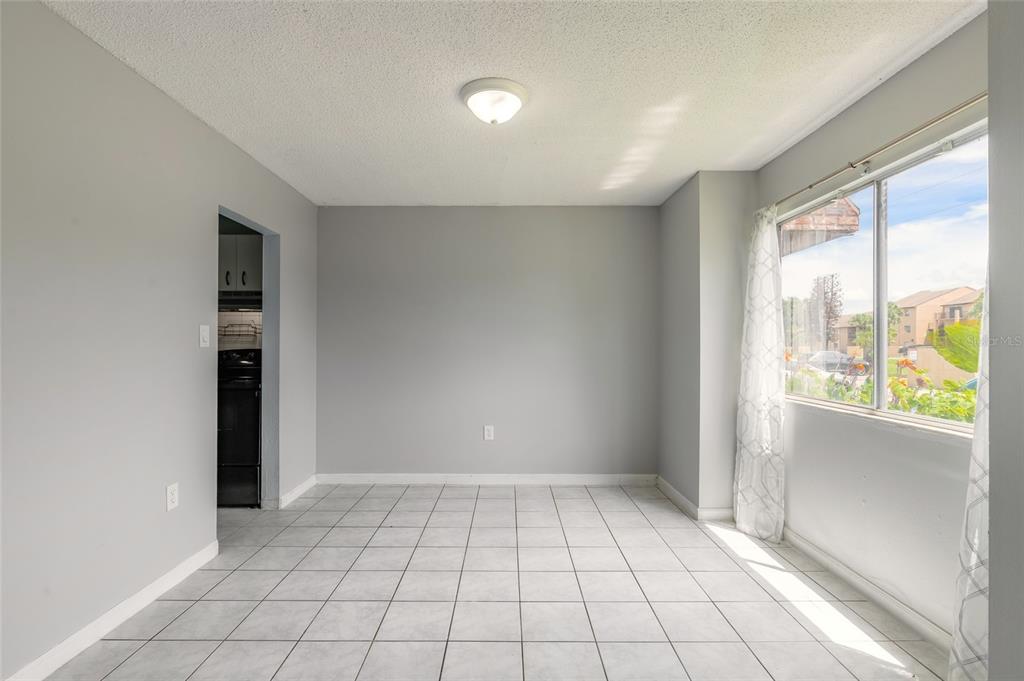 An empty room with light blue walls, white tile flooring, and a large window — 5060 DOWNING STREET UNIT 6, ORLANDO, FL