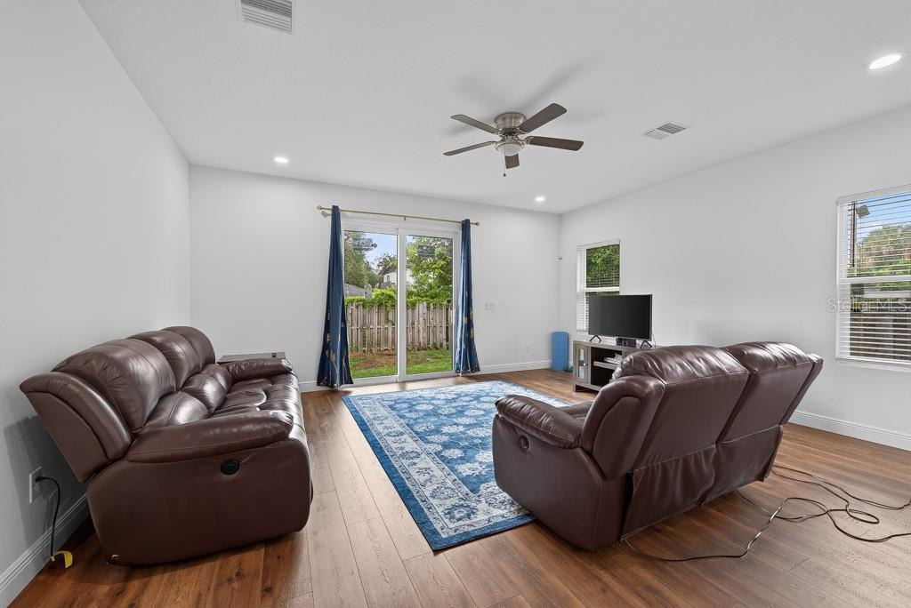 A living room features brown leather sofas, a blue patterned area rug, and sliding glass doors — 8118 N SEMMES STREET, TAMPA, FL