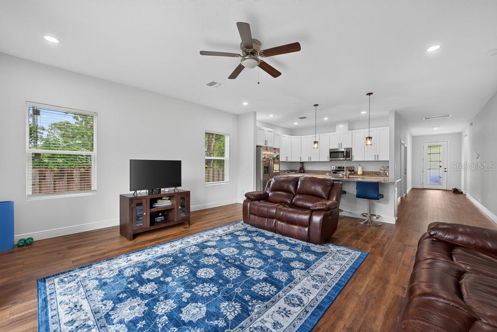 An open-concept living room and kitchen featuring wood-look flooring, a blue rug, and leather furniture — 8118 N SEMMES STREET, TAMPA, FL