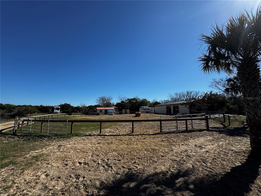 A fenced dirt paddock with a hay bale and outbuildings under a clear blue sky — 3100 GRANTLINE ROAD, MIMS, FL