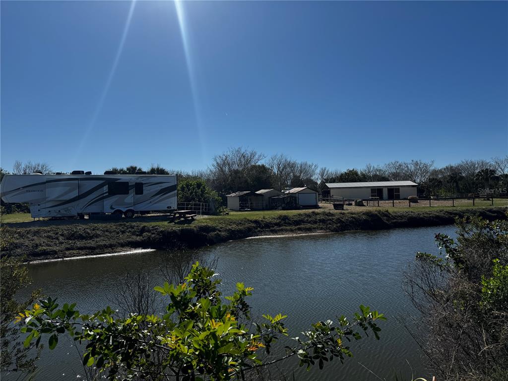 A recreational vehicle is parked near a small pond with outbuildings in the background — 3100 GRANTLINE ROAD, MIMS, FL