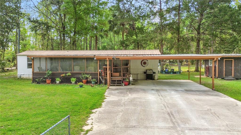 A mobile home with a large screened-in porch and an attached carport sits on grass — 3650 SE 176TH PLACE, INGLIS, FL