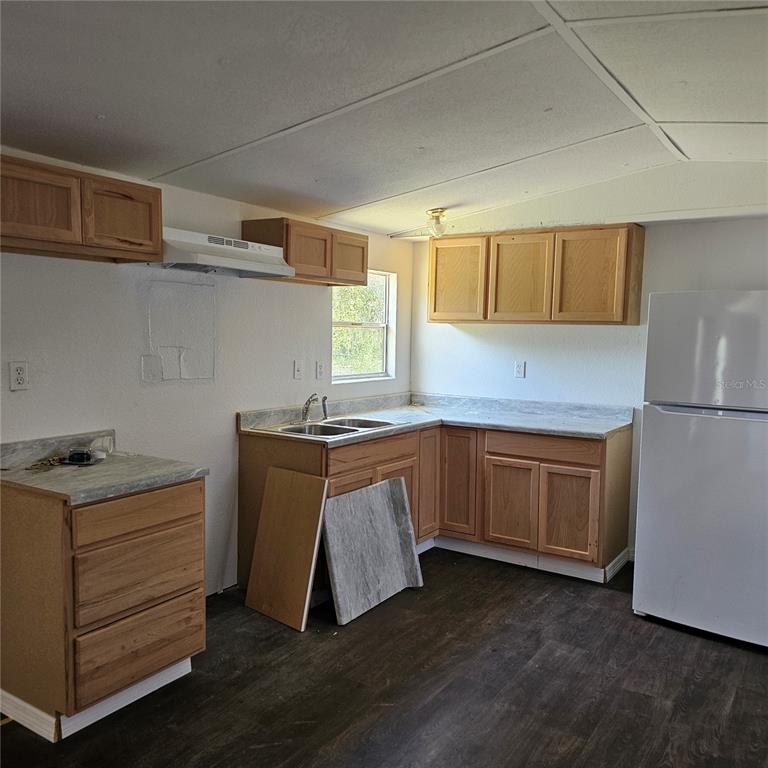 A kitchen features light wood cabinets, laminate countertops, a white refrigerator, and dark flooring — 2603 INCE DRIVE, RUSKIN, FL