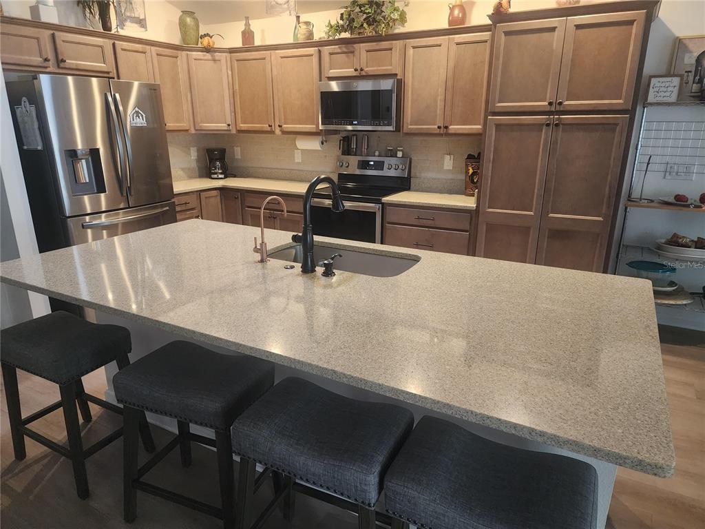 A kitchen features light wood cabinets, granite countertops, a large island with seating, and stainless appliances — 7591 MERGAERT LANE, MIDDLETON, FL