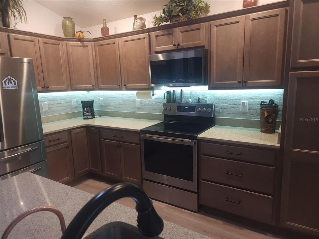 A kitchen features wood cabinets, stainless steel appliances, a stone-look backsplash, and granite countertops — 7591 MERGAERT LANE, MIDDLETON, FL