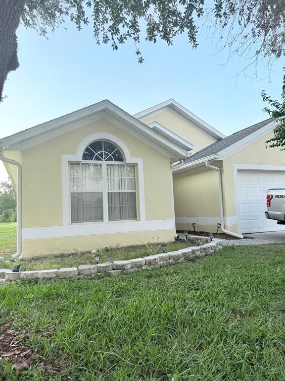 A yellow single-story house features a large arched window and a stone garden border — 16425 GOLDEN EAGLE BOULEVARD, CLERMONT, FL