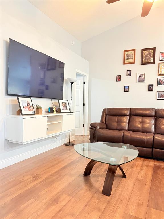 A living room features a wall-mounted television, white floating console, brown leather sofa, and wood flooring — 16425 GOLDEN EAGLE BOULEVARD, CLERMONT, FL