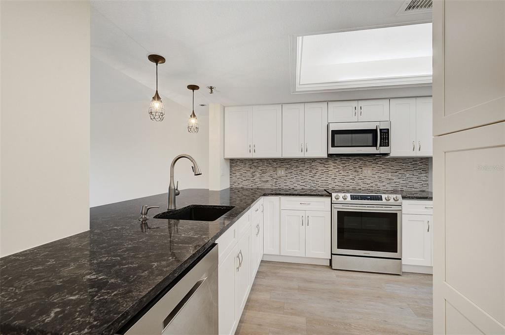 A kitchen features white cabinets, dark granite countertops, stainless steel appliances, and a tile backsplash — 7204 JESSIE HARBOR DRIVE UNIT 7204, OSPREY, FL