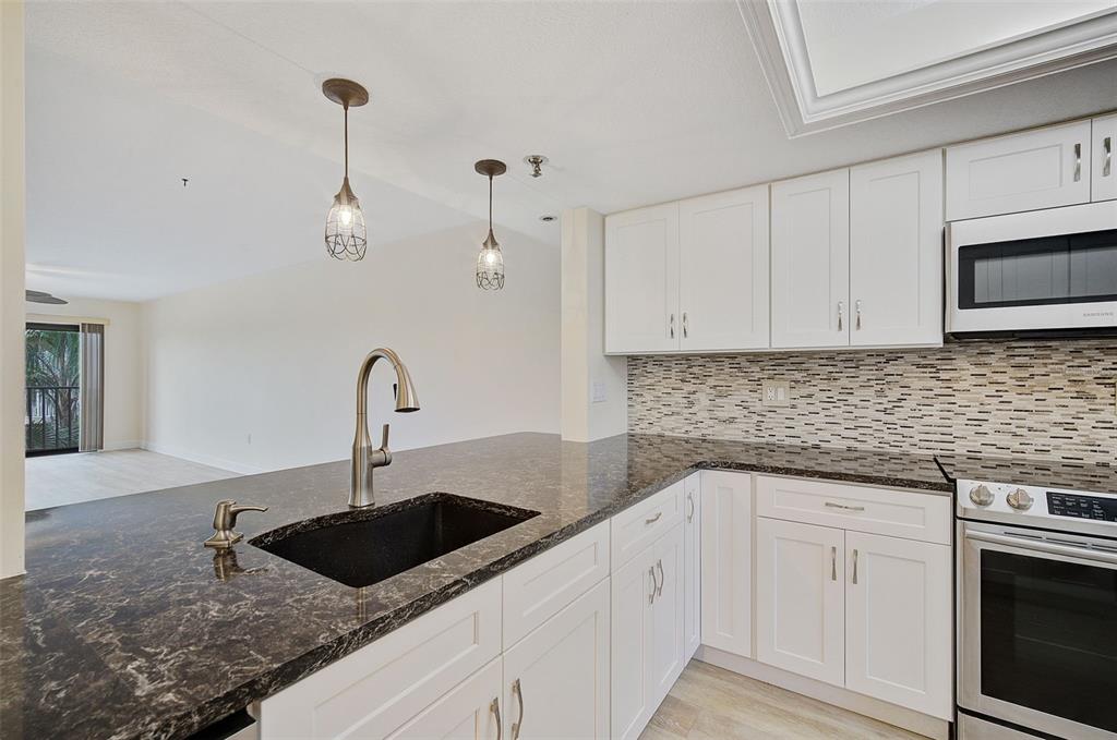 A kitchen features white cabinets, dark granite countertops, a black sink, and stainless steel appliances — 7204 JESSIE HARBOR DRIVE UNIT 7204, OSPREY, FL