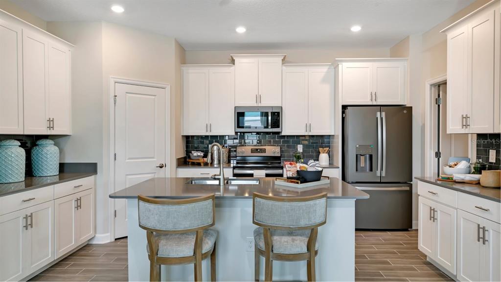 A kitchen features white cabinets, a gray island with seating, and stainless steel appliances — 3273 WHOLENESS WAY, CLERMONT, FL