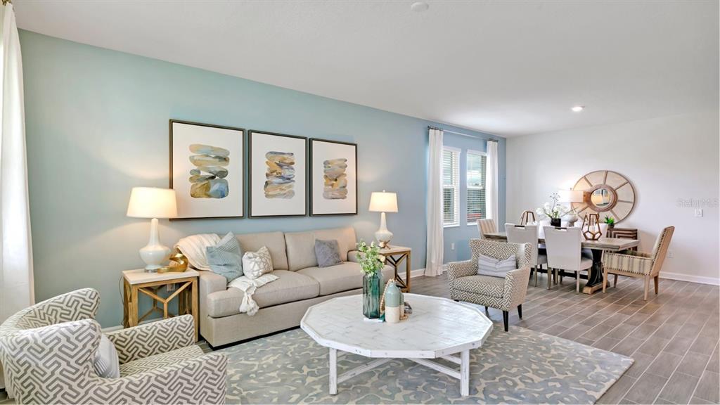 A living room with a light blue wall, beige sofa, patterned armchairs, and dining area — 3273 WHOLENESS WAY, CLERMONT, FL